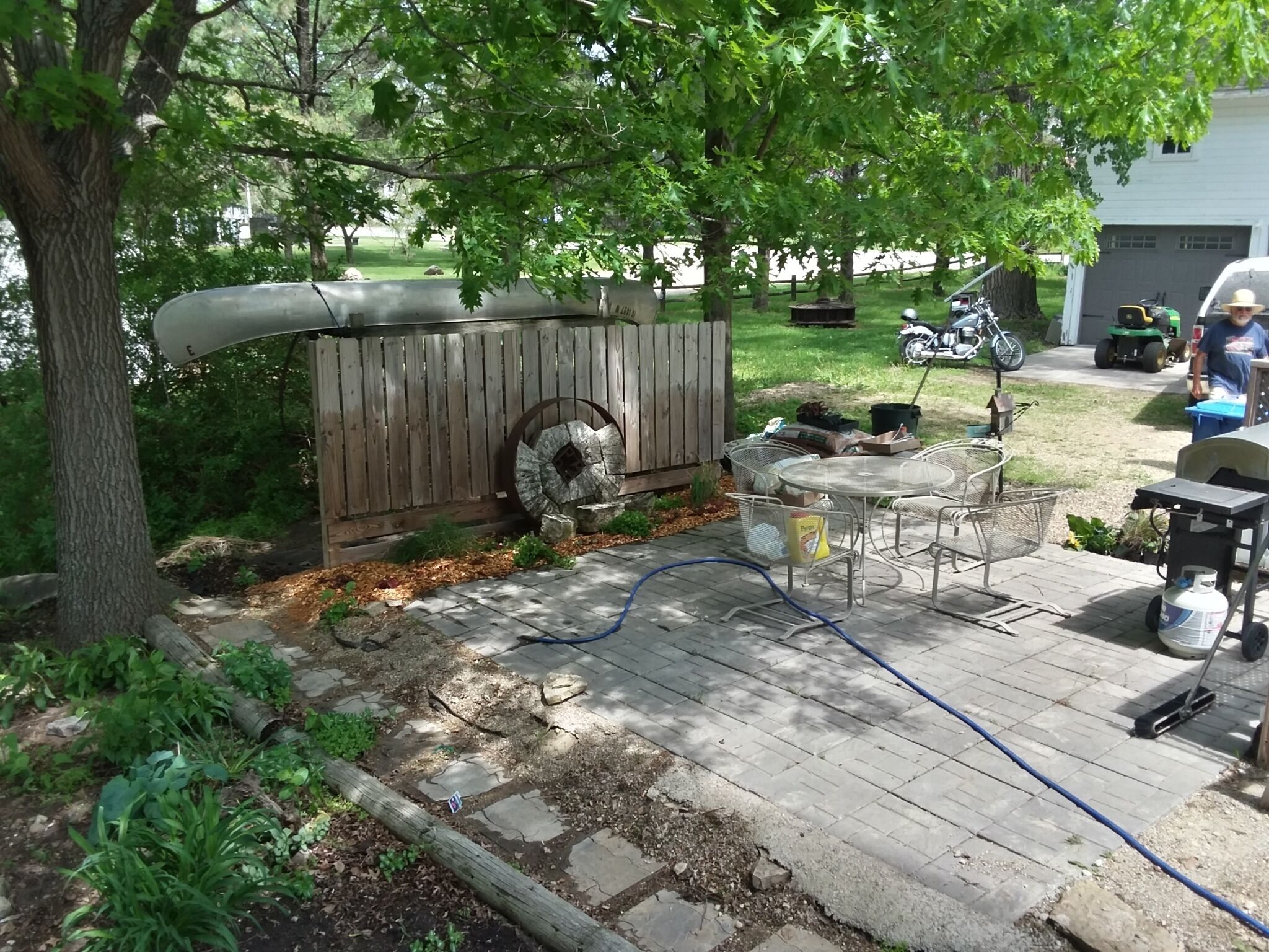 Een achtertuin met een houten terras, een metalen tafel en een barbecue.