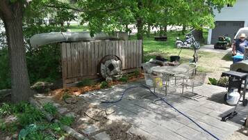 Een achtertuin met een houten terras, een metalen tafel en een barbecue.