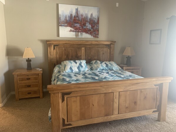 A bedroom with a wooden bed, two nightstands, a wall-mounted painting, and a carpeted floor. - Resort style backyard (Lake Havasu City)