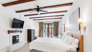 Un dormitorio amplio con una cama grande, un televisor montado en la pared, una chimenea y un ventilador de techo.