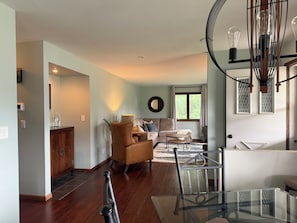 A modern living room with a glass coffee table, a sofa, a chair, and a dining area with a glass table.