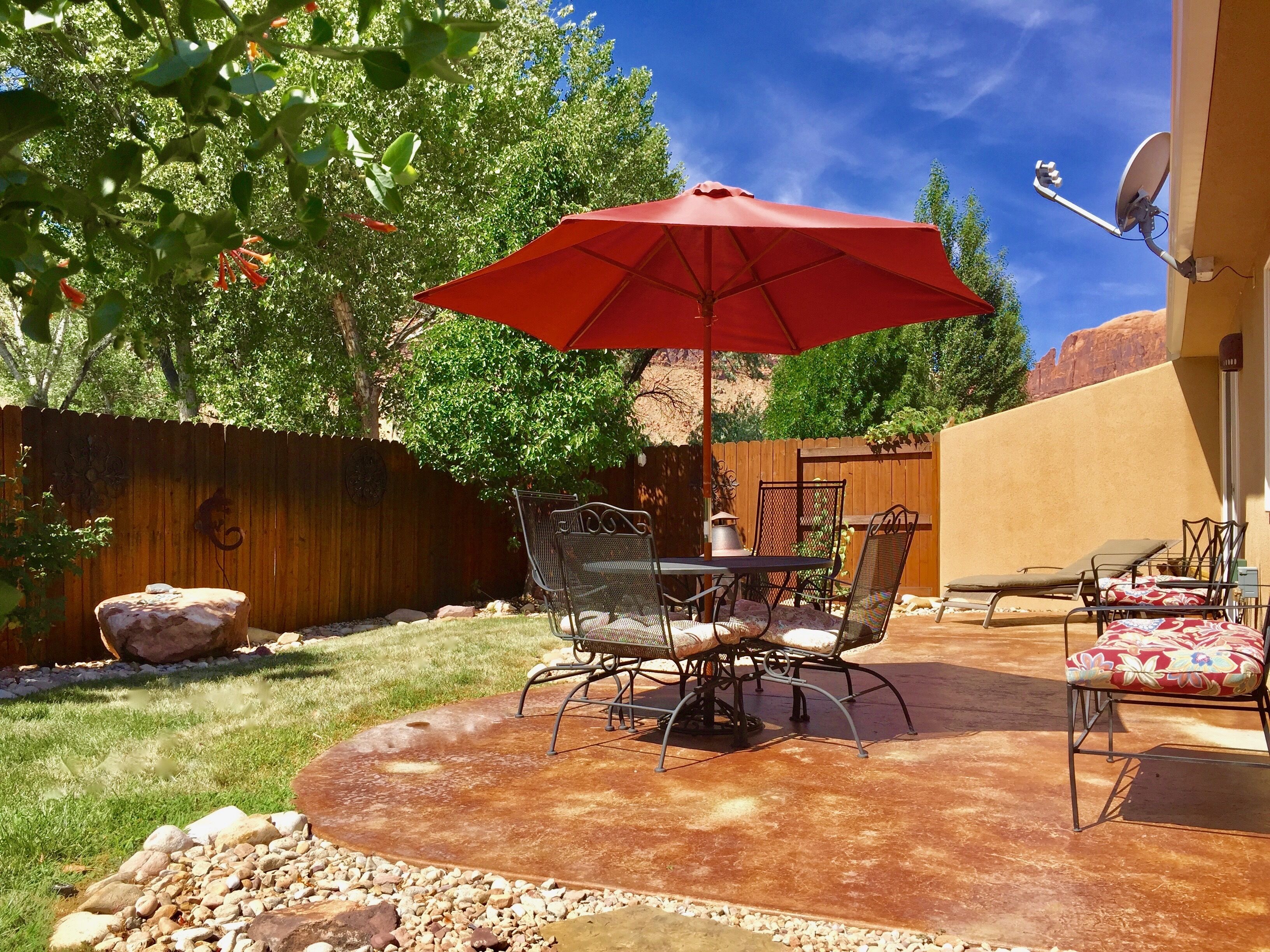 Une terrasse extérieure avec un parasol rouge, des chaises en métal et une table.