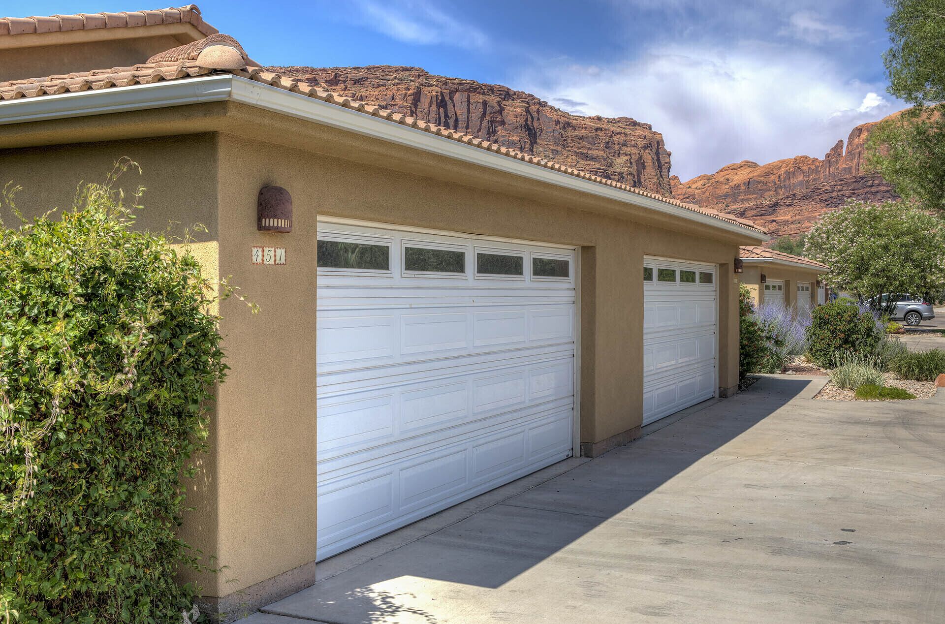 Un immeuble résidentiel avec deux portes de garage, le numéro « 451 » peint sur le mur, et un paysage montagneux en arrière-plan.