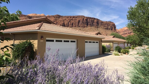 A residential building with a garage, surrounded by lavender plants and a desert landscape with red rock formations. - In Town Near Main Street!  Single Level With Garage - Private Gated Yard (Moab)