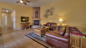 A living room with a fireplace, leather sofa, television, and a ceiling fan. - In Town Near Main Street!  Single Level With Garage - Private Gated Yard (Moab)