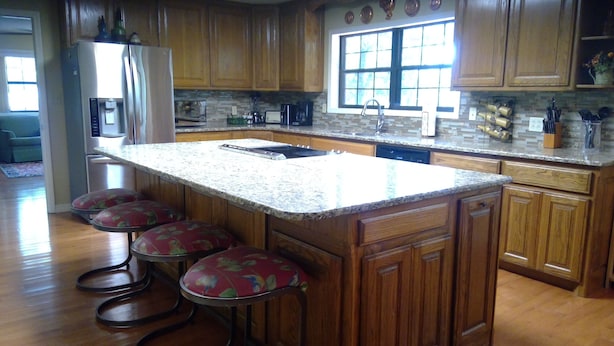 A kitchen with wooden cabinets, a granite countertop, and a stainless steel refrigerator. There are four bar stools with floral upholstery. - Family Friendly Lakefront House on Greers Ferry Lake 1/2 mile to Marina, Boating (Clinton)