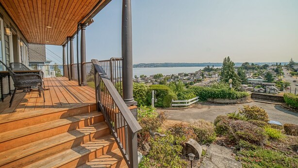 A wooden deck with a railing, a staircase, and a view of a town and water body.