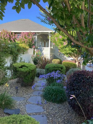 A well-maintained garden with a stone pathway leading to a house with a porch.