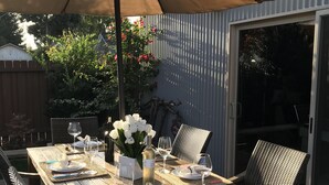 An outdoor dining area with a wooden table set for four, surrounded by wicker chairs, under a large umbrella.