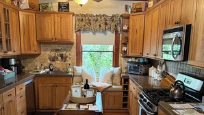 A kitchen with wooden cabinets, a gas stove, a microwave, and a window with a view of greenery.