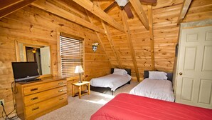 Ein Schlafzimmer in einer Holzhütte mit zwei Betten, einem Schminktisch, einem Fernseher und einem Fenster mit Jalousien.