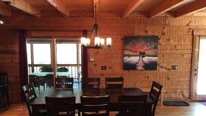 Ein Holzinterieur mit einem Esstisch und Stühlen, einem Bild an der Wand und einem Fenster mit Vorhängen.
