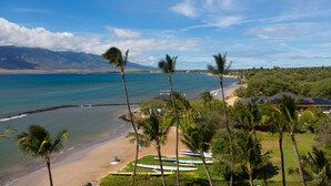 A beach with palm trees, a sandy shore, and a view of the ocean and mountains in the distance. - Gorgeous Oceanfront Condo Steps From The Beach, Air Conditioned, Free Wi-Fi (Kihei)