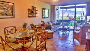 A spacious living area with a glass dining table, wicker chairs, a sofa, and a ceiling fan. - Gorgeous Oceanfront Condo Steps From The Beach, Air Conditioned, Free Wi-Fi (Kihei)