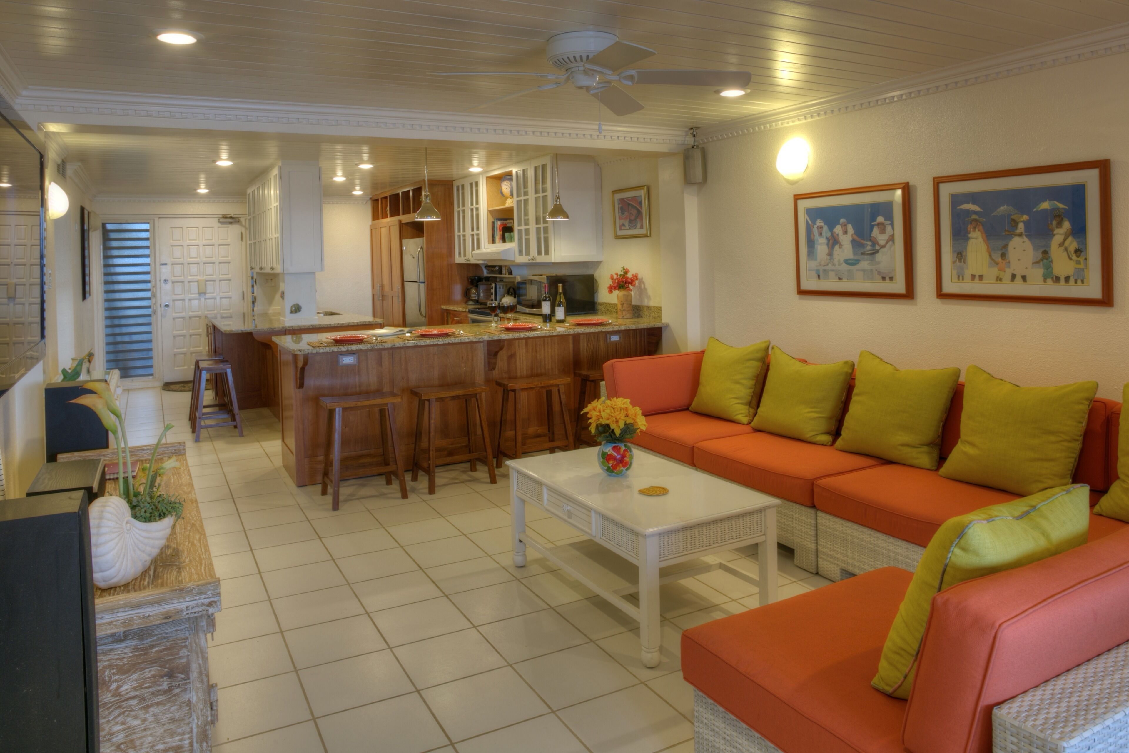 A spacious living area with a kitchen in the background, a large orange sofa with green cushions, and a white coffee table.