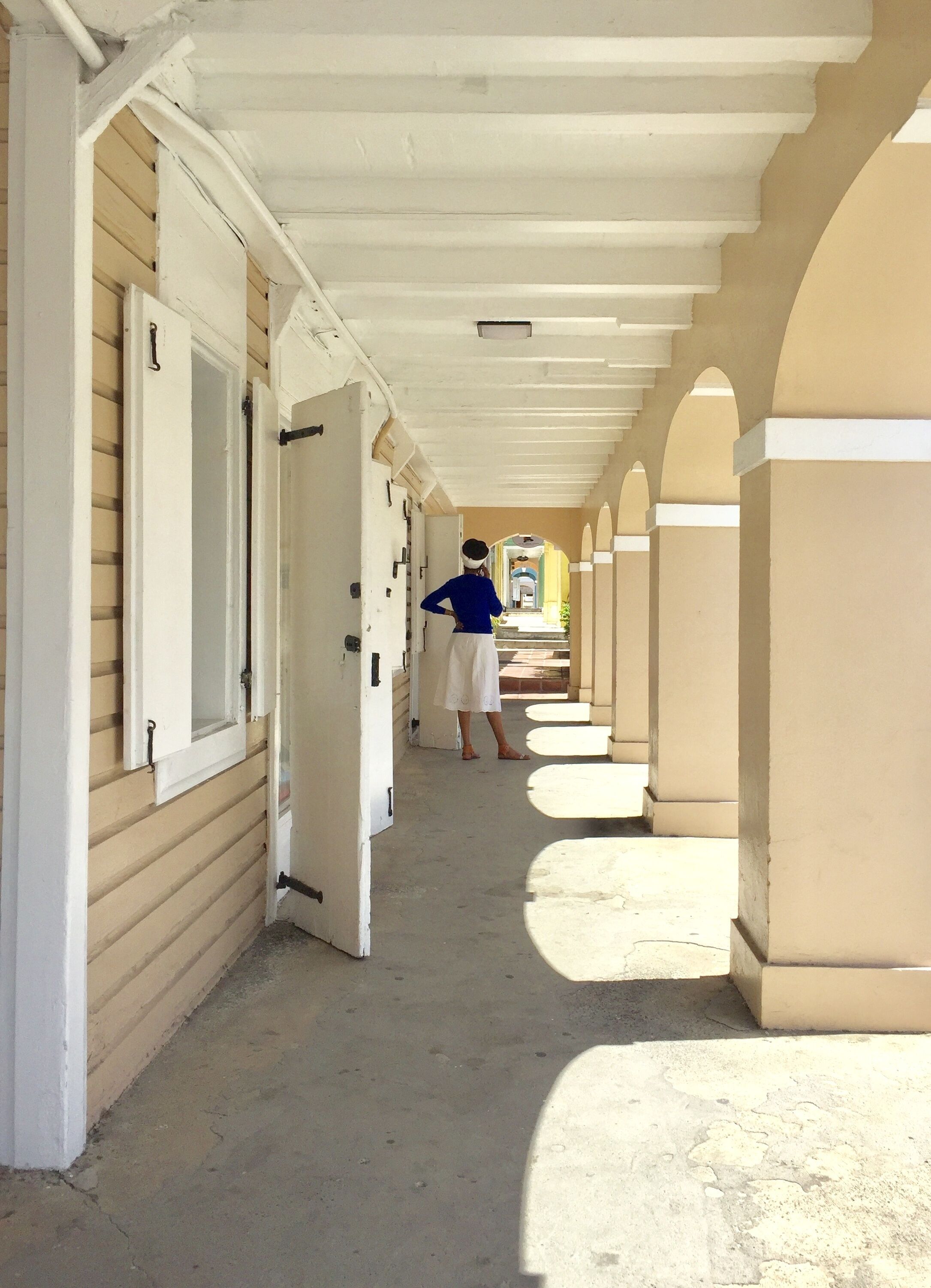 A corridor with open doors leading to rooms, a person standing in the distance, and a view of a building in the background.