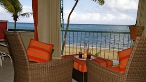 A balcony with wicker chairs and orange cushions, overlooking a beach and the ocean.