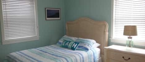 A bedroom with a bed, a nightstand, a lamp, and a window with blinds.
