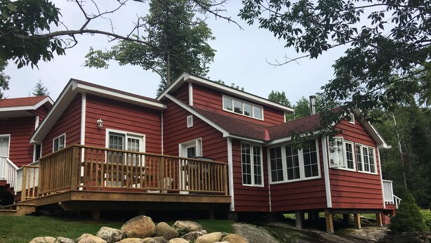 A two-story house with a wooden deck and a stone wall in front. - Muskoka Cottage Living  (Huntsville)