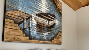A room with a bed, a striped pillow, and a large artwork depicting a boat on a wooden wall. - Muskoka Cottage Living  (Huntsville)
