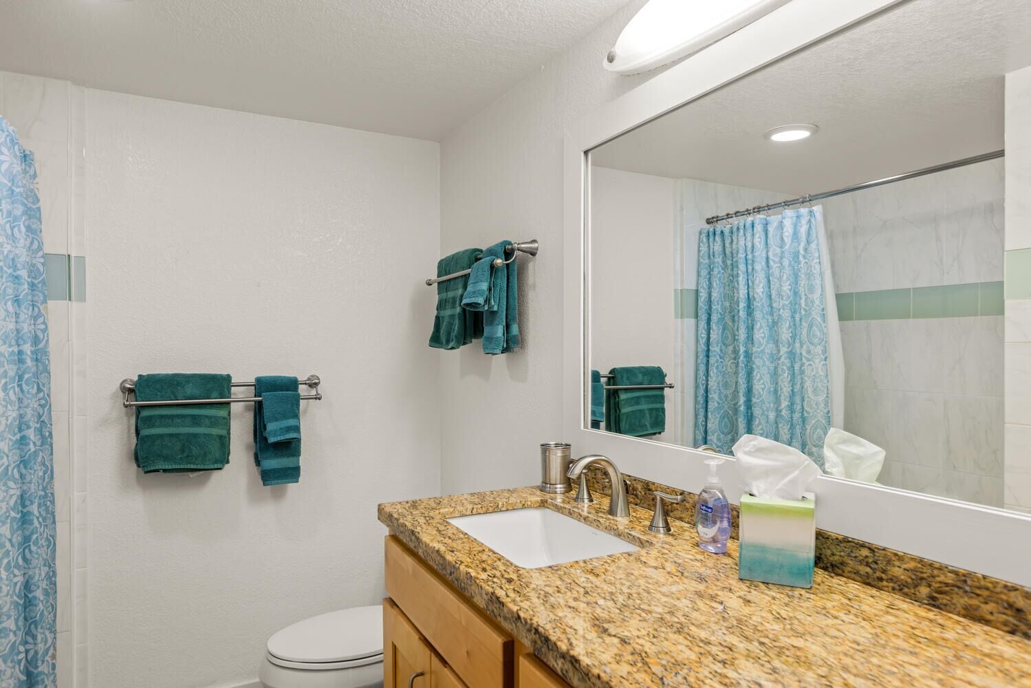 A bathroom with a granite countertop, a sink, a mirror, and two towels hanging on towel racks.