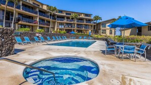 A hotel with a swimming pool, lounge chairs, and a blue umbrella.