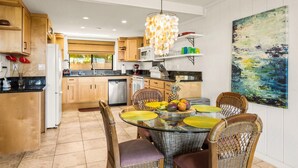 A modern kitchen with wooden cabinets, a dining area with wicker chairs, and a large abstract painting on the wall.
