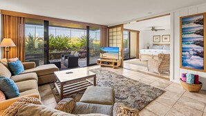 A spacious living area with a large sliding glass door leading to a balcony, a flat-screen TV, a comfortable sofa, and a dining area.