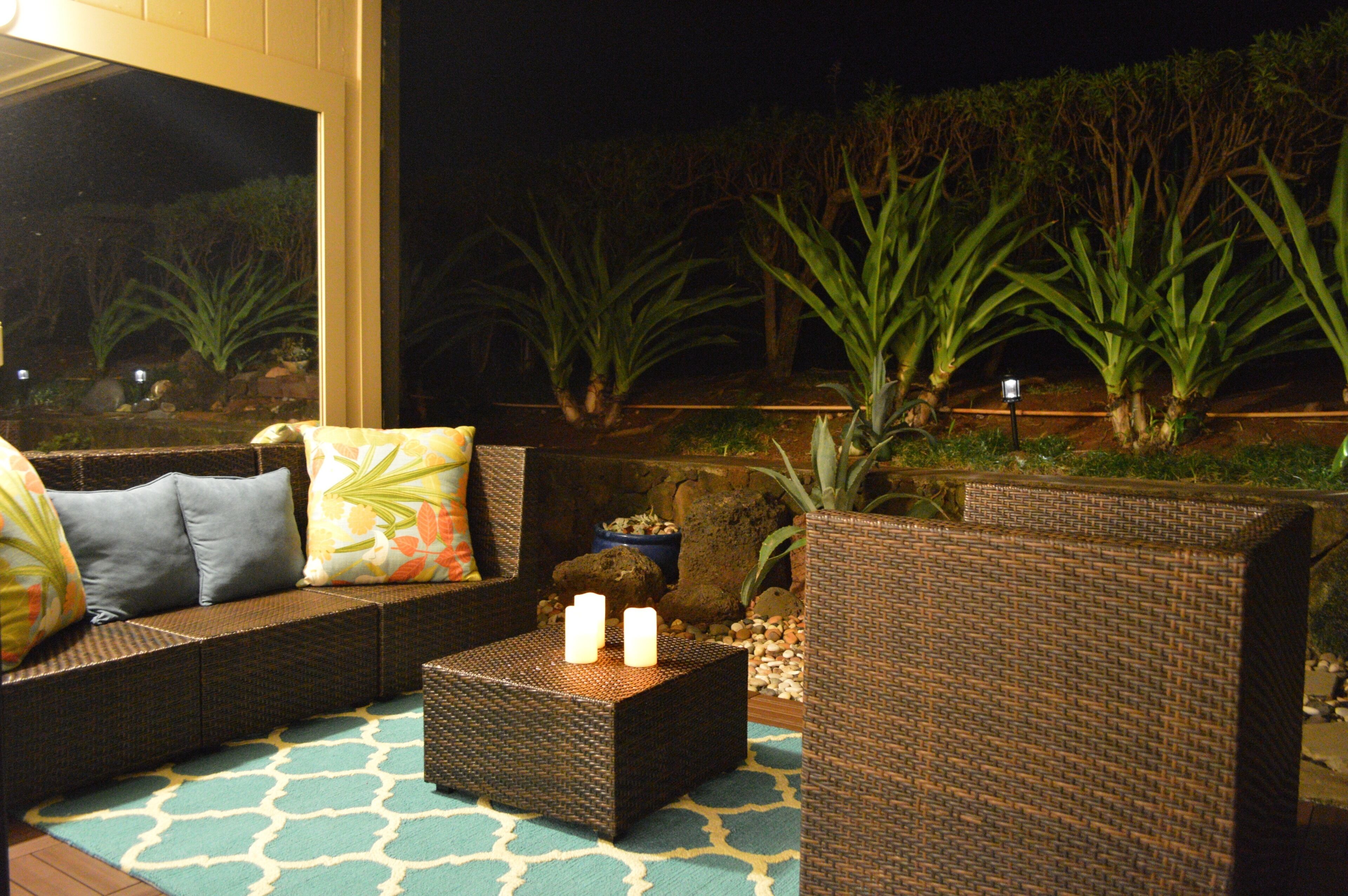 An outdoor seating area with wicker furniture, cushions, and a small table with candles.