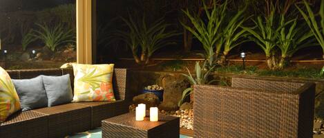 An outdoor seating area with wicker furniture, cushions, and a small table with candles.