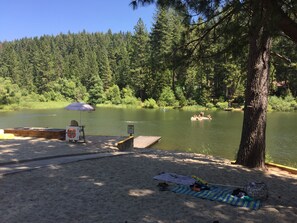 Ein Campingplatz am Seeufer mit Anlegesteg, Picknicktisch und Strand, Handtücher und Taschen sind vorhanden.