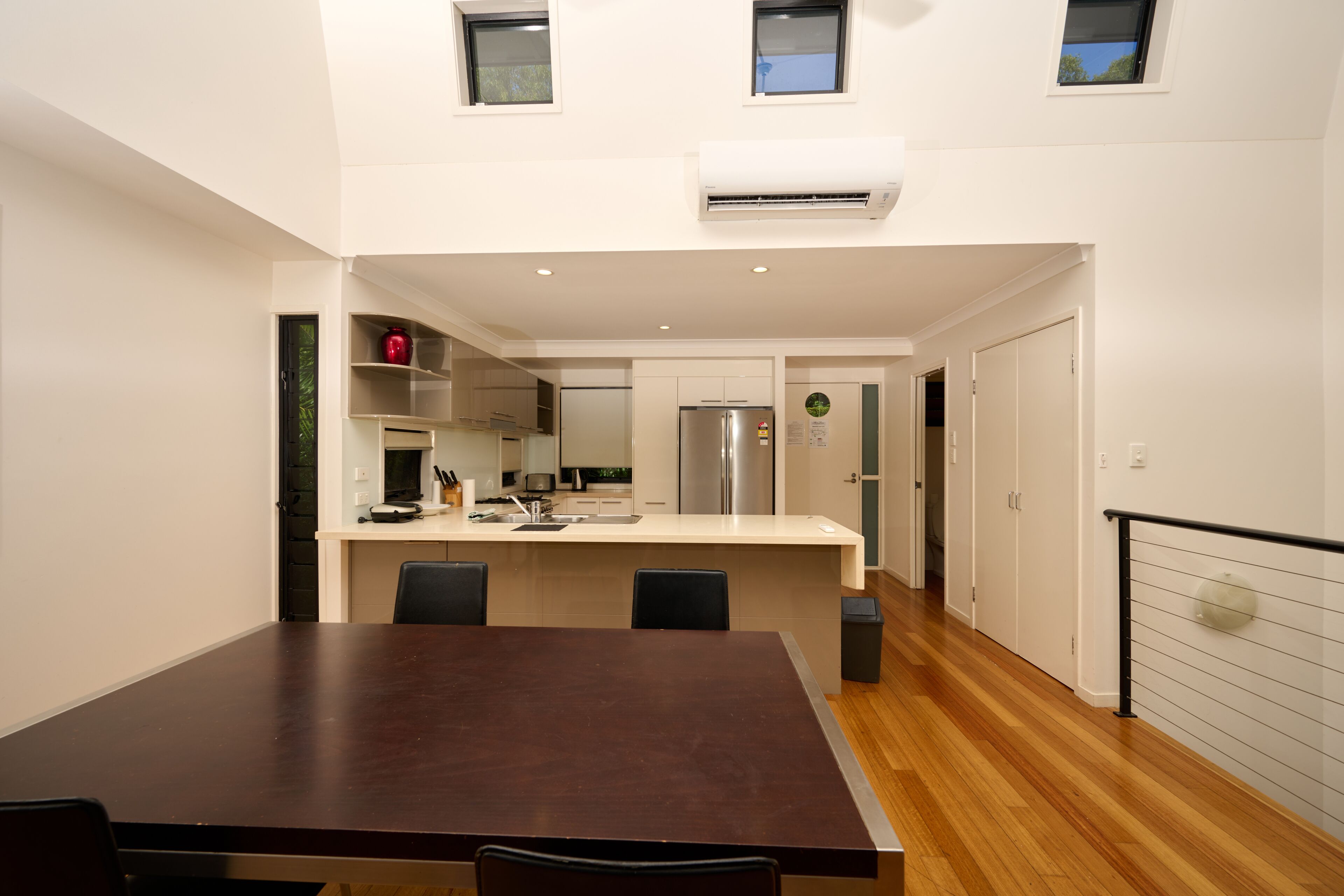 Una cocina moderna con armarios blancos, un refrigerador de acero inoxidable y una mesa de comedor de madera.