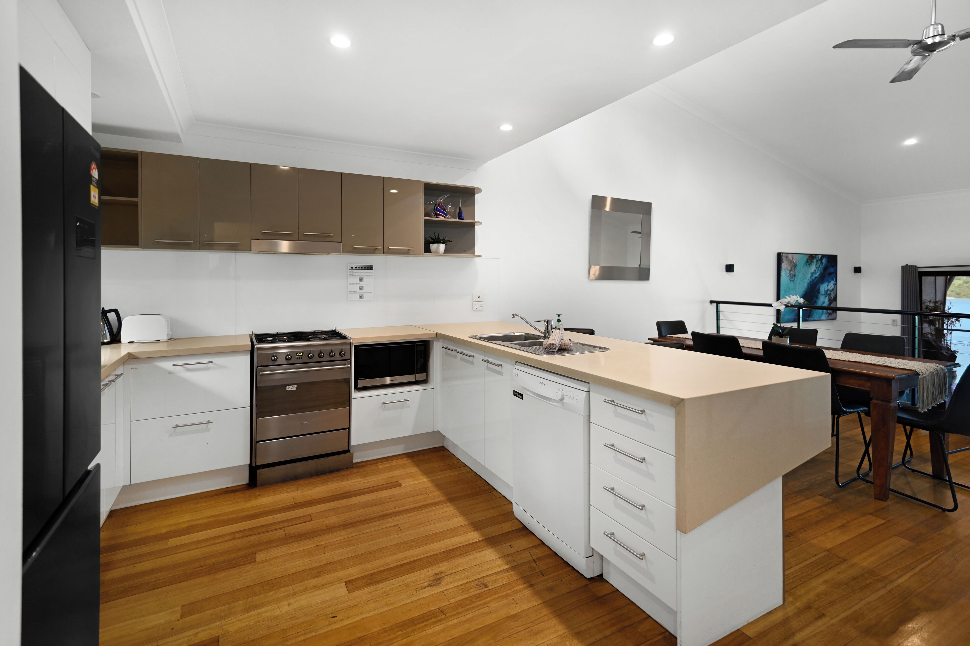 A modern kitchen with white cabinets, stainless steel appliances, and a wooden floor.