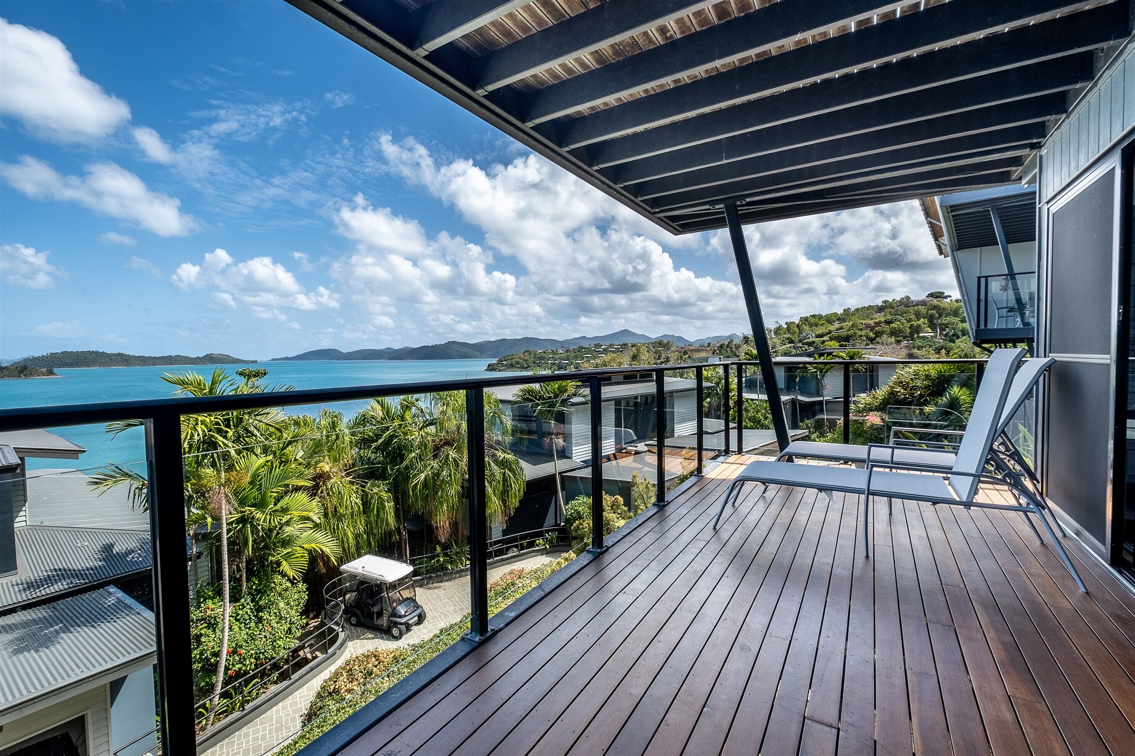 A wooden deck with a view of a coastal landscape, including a body of water and distant hills.