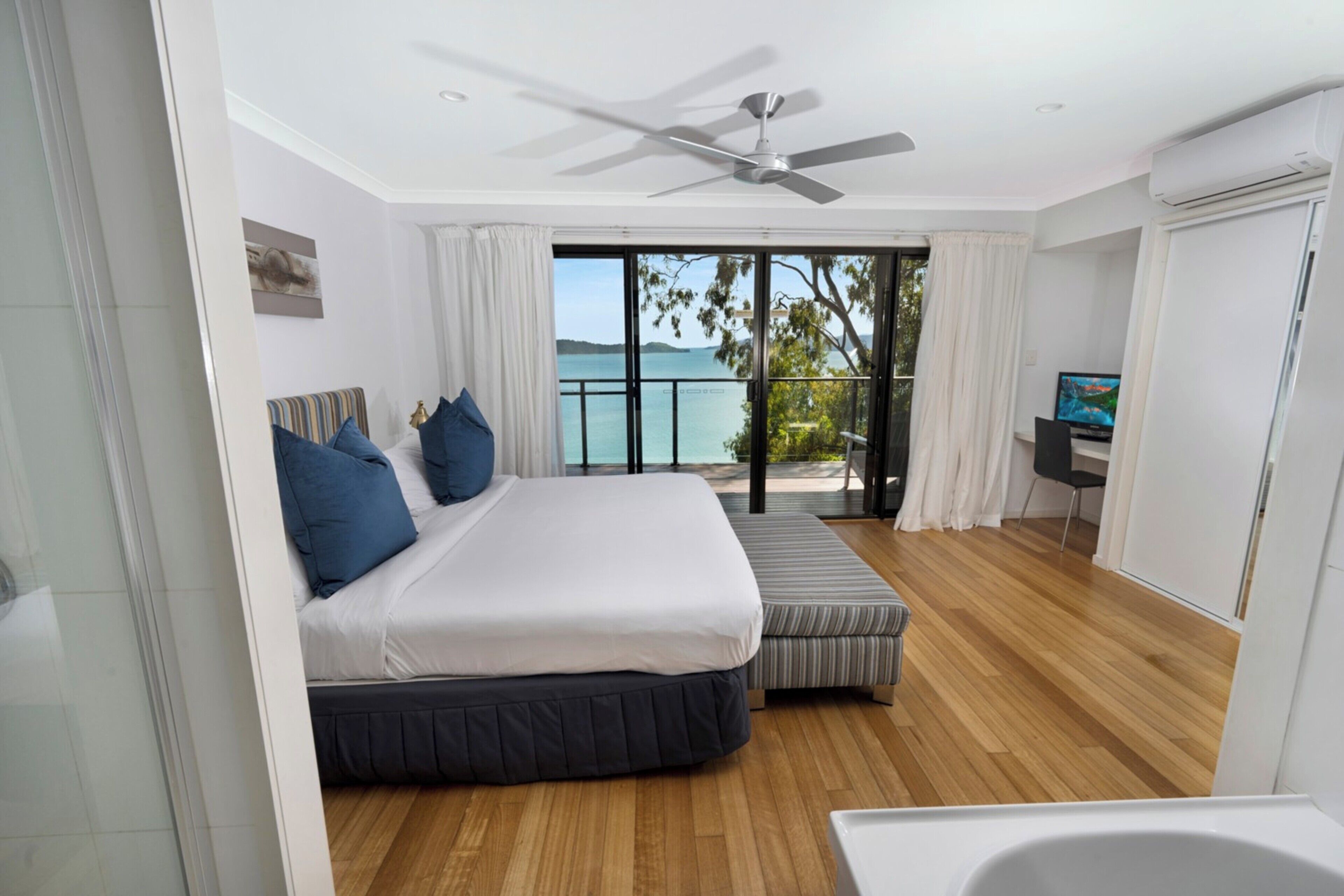 Un dormitorio con una cama grande, un sofá pequeño, un ventilador de techo y vista al mar.