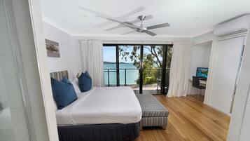 Un dormitorio con una cama grande, un sofá pequeño, un ventilador de techo y vista al mar.