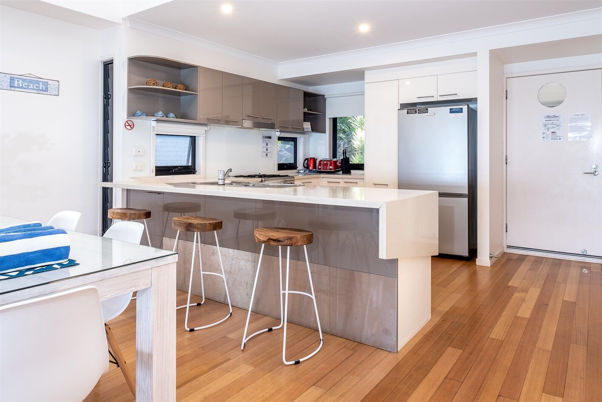 A modern kitchen with a central island, bar stools, a refrigerator, and a dining area with a table and chairs.