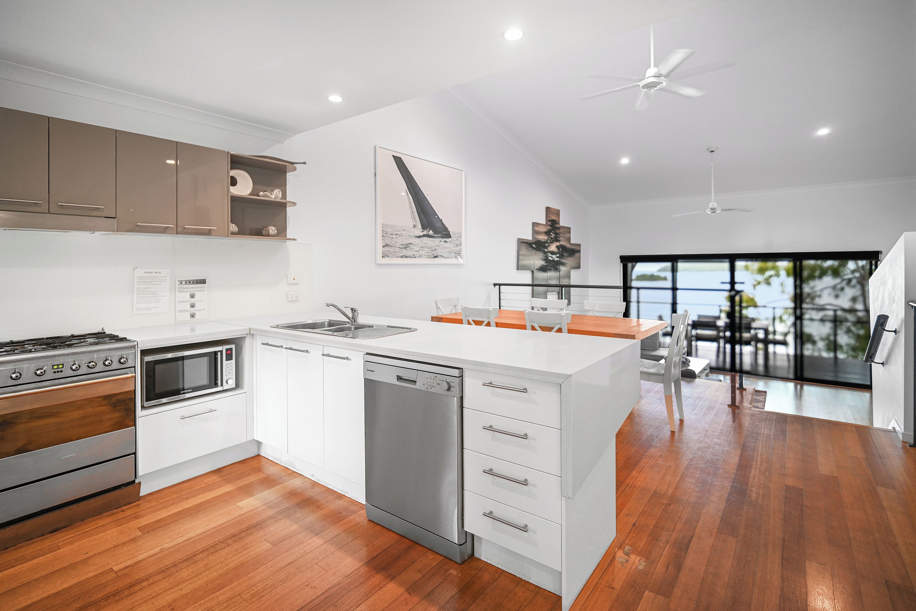A modern kitchen with white cabinetry, stainless steel appliances, and a wooden floor.