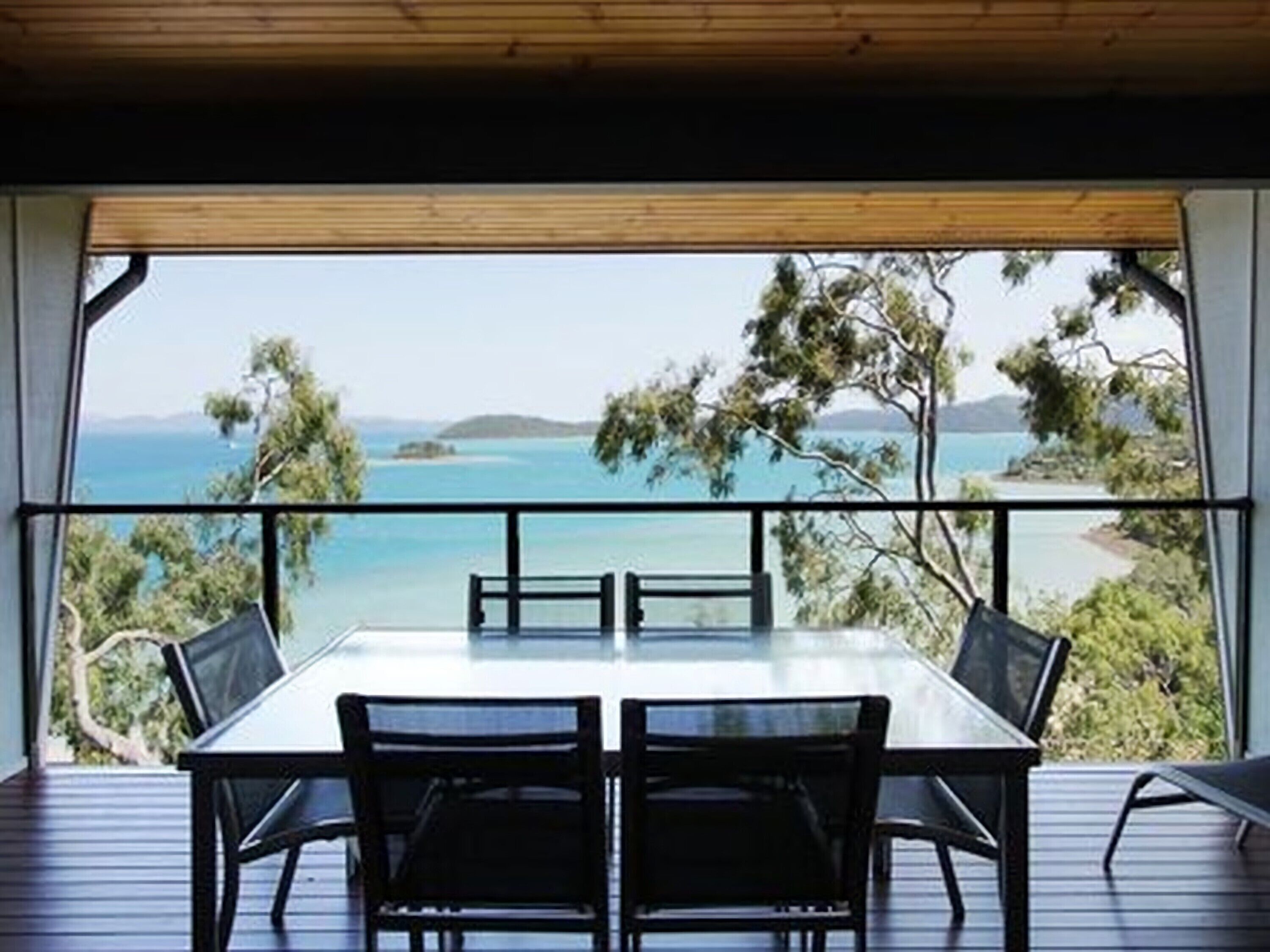A dining area with a table and chairs, overlooking a scenic view of the sea and greenery.