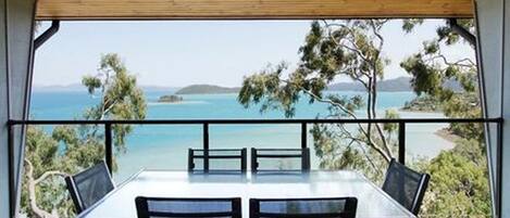 A dining area with a table and chairs, overlooking a scenic view of the sea and greenery.