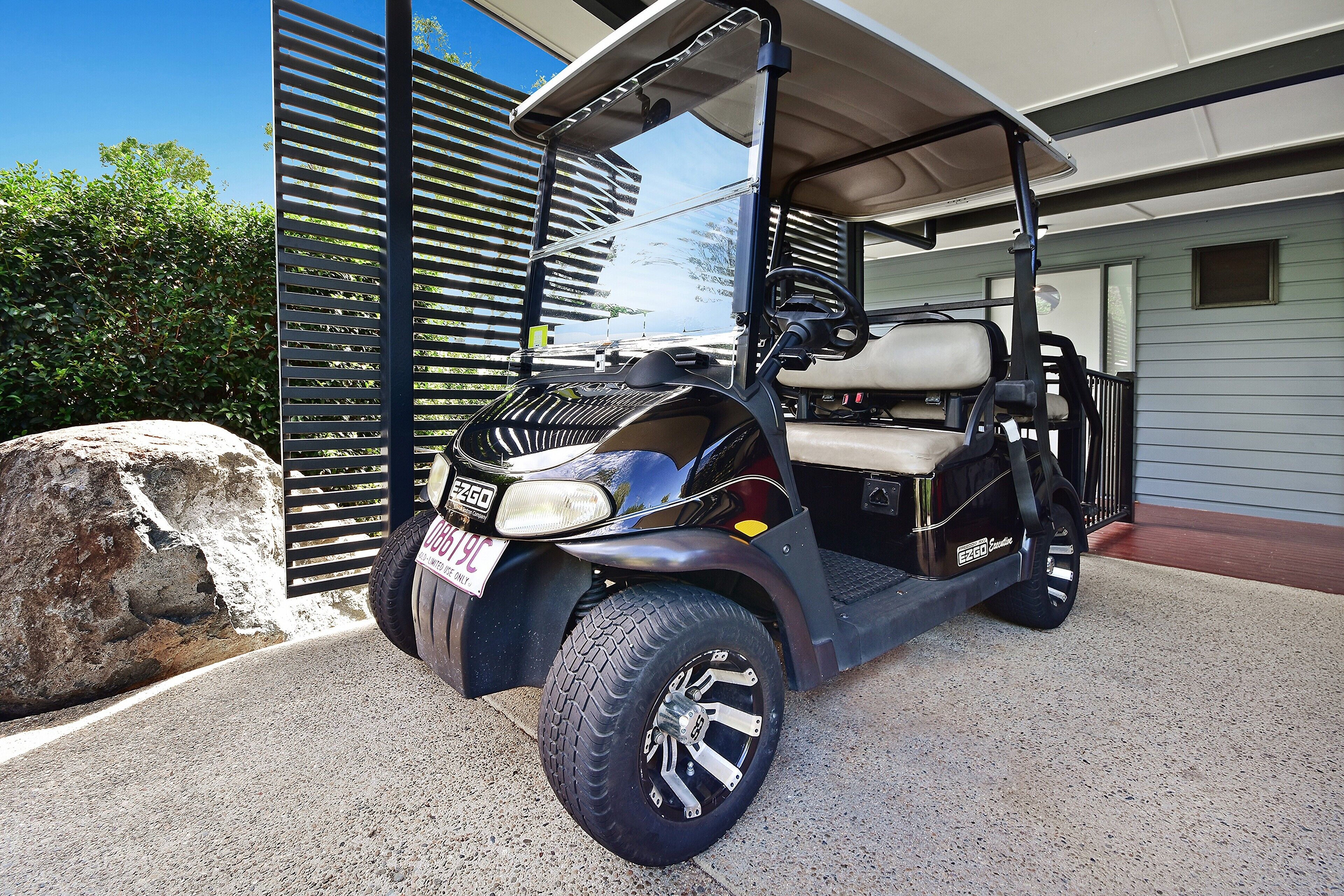 Ein Golfwagen vor einem Haus mit einem großen Felsen und einem Metallzaun.