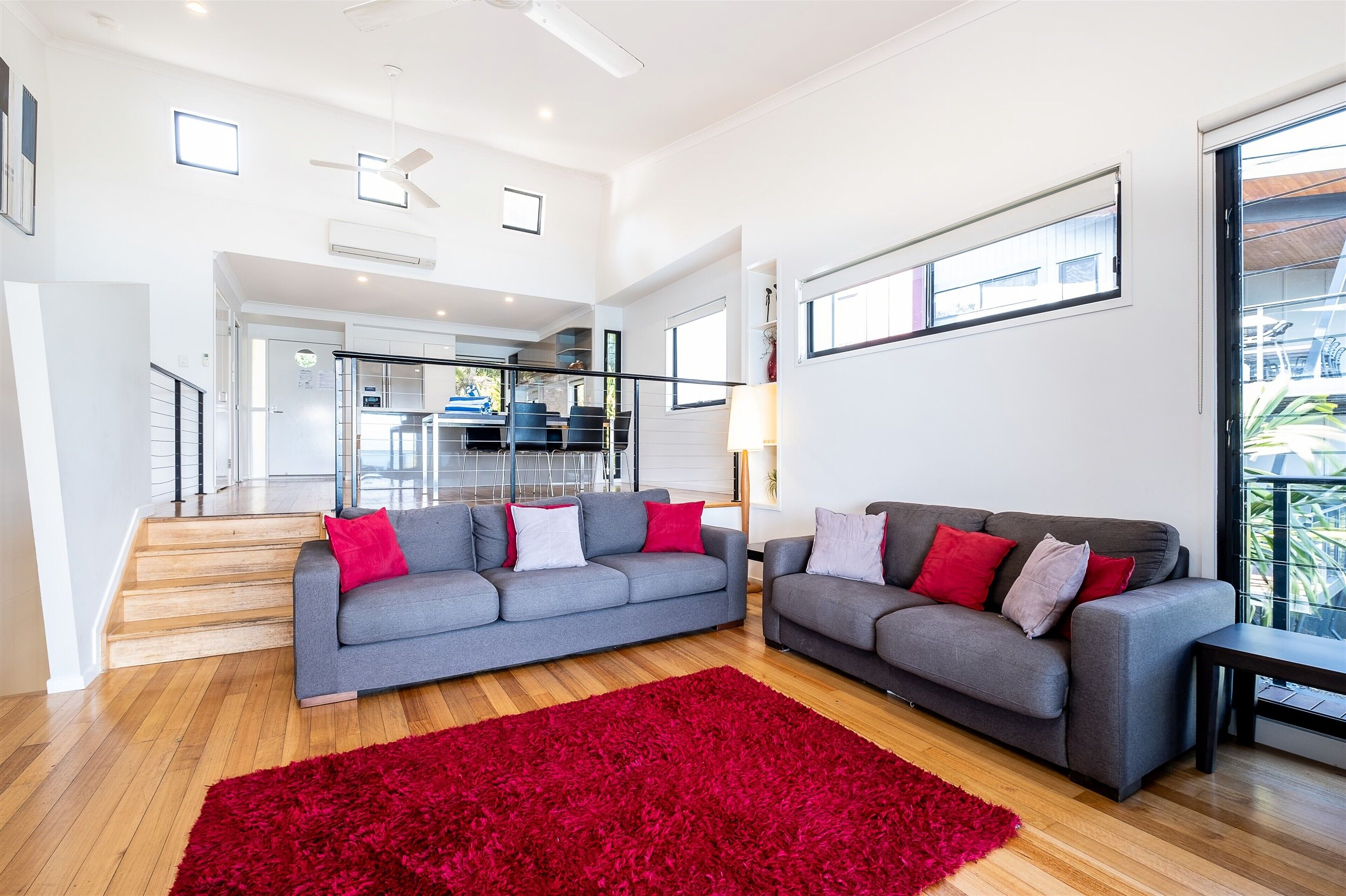 A spacious living area with two grey sofas, a red rug, and a staircase leading to an upper level.