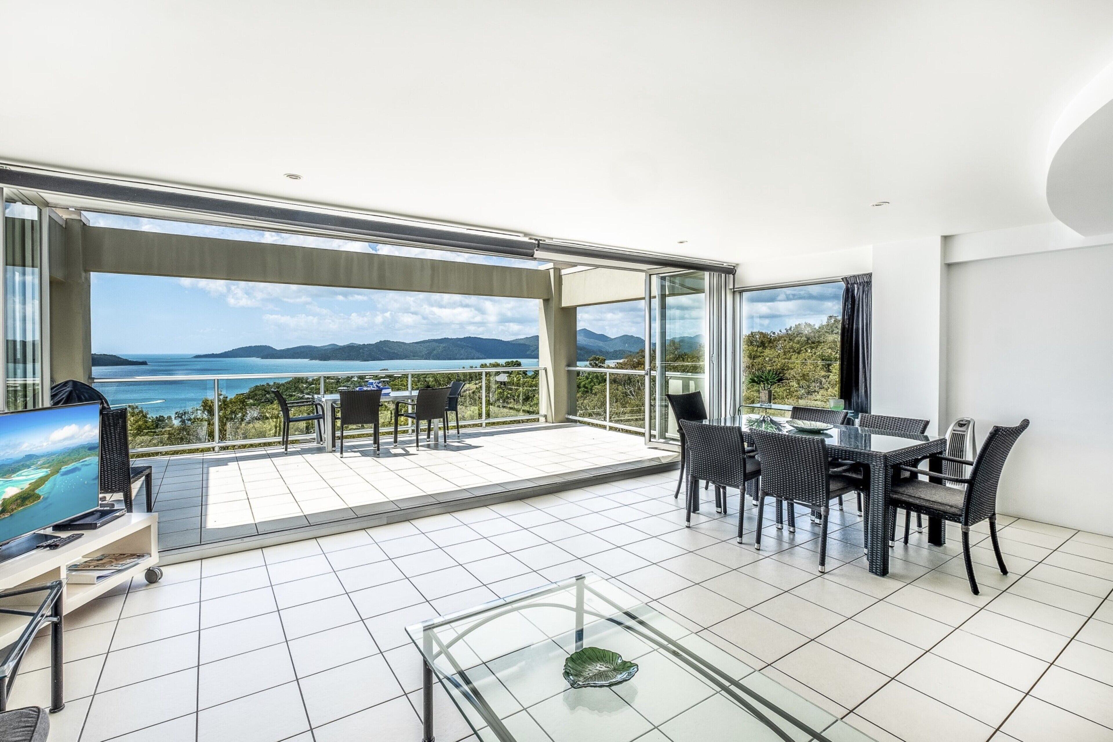 A spacious balcony with a glass door, a dining area with a table and chairs, and a television on a stand.