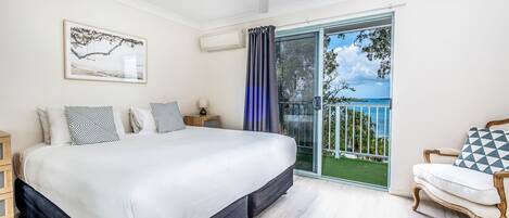 A bedroom with a large bed, a ceiling fan, a view of the outdoors through a sliding glass door, and a chair with a cushion.