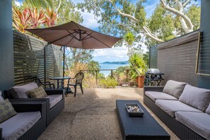 A patio with wicker furniture, a table, and an umbrella. - Sunset Waters Apartments (Whitsundays)