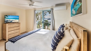Un dormitorio con cama, cómoda, televisión, balcón con vistas y ventilador de techo.