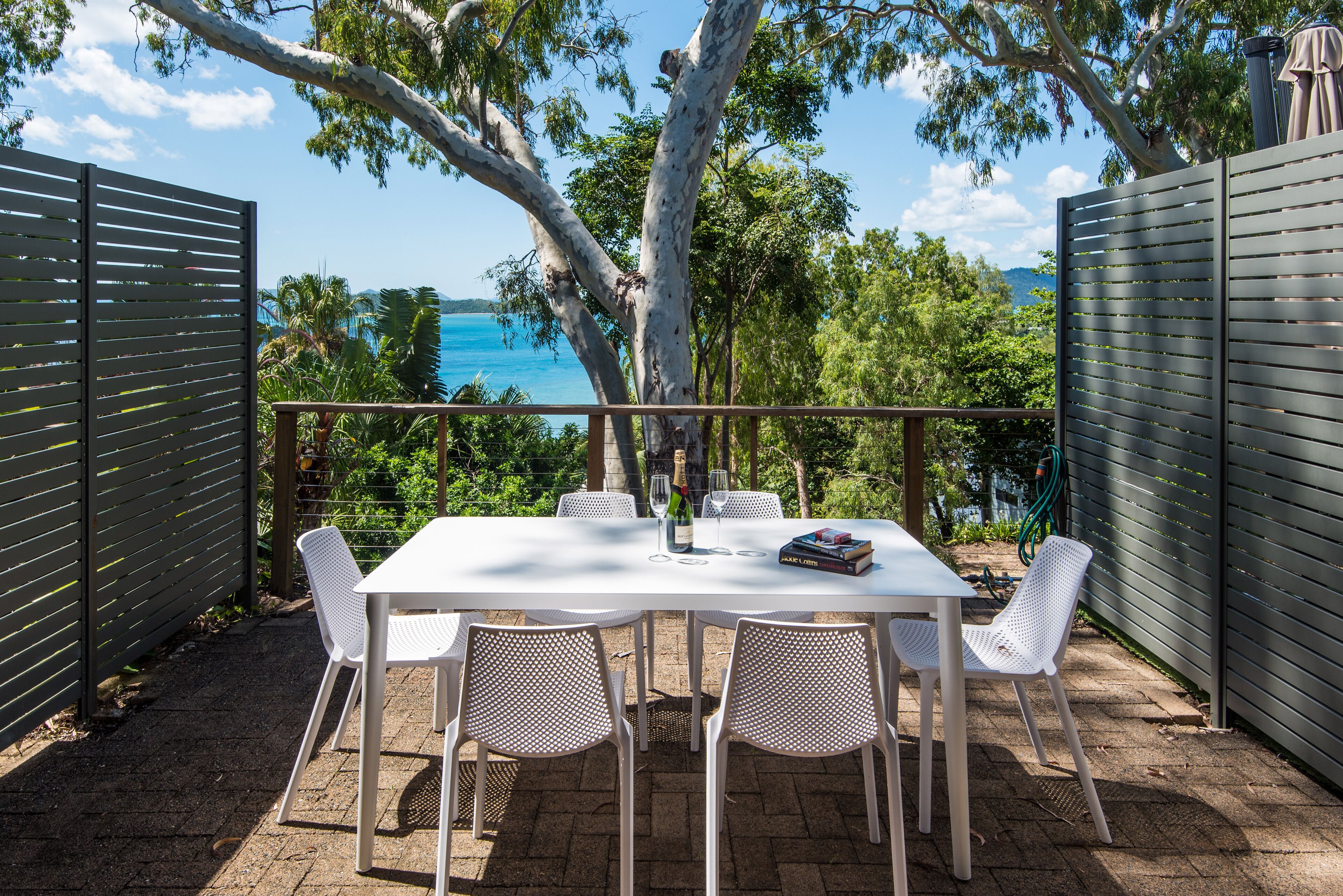 A patio with a table and chairs, a book, and a bottle of champagne.