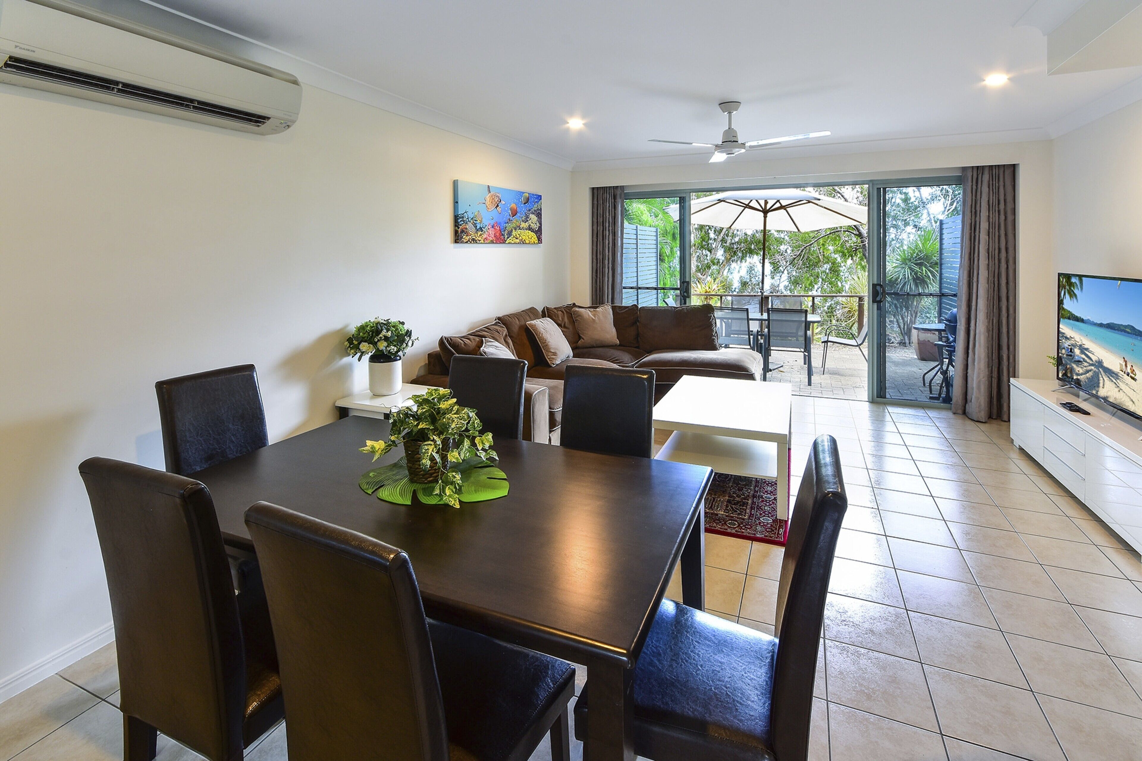 A dining area with a table and chairs, a sofa, and a television on a stand.