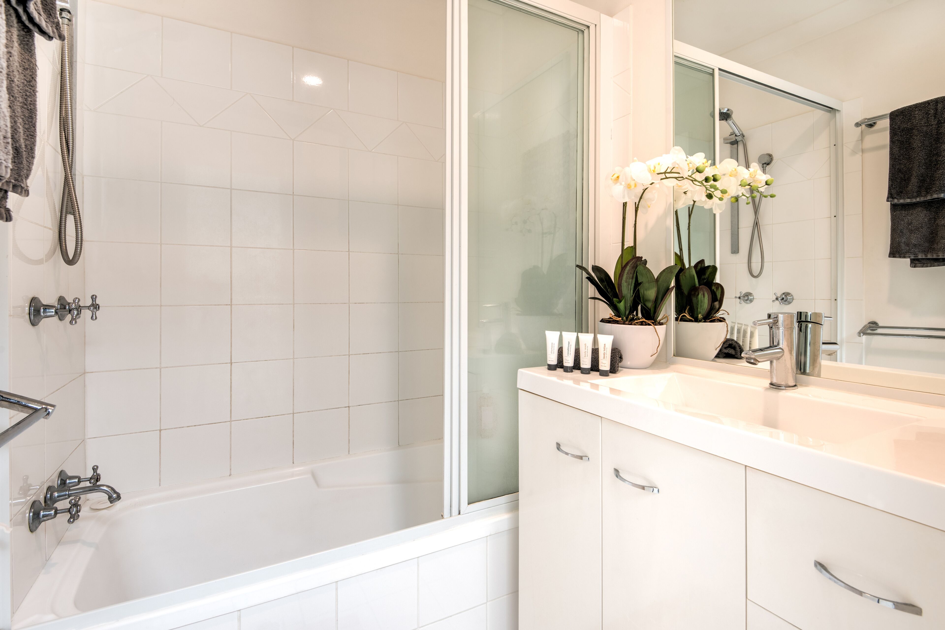 A modern bathroom with a bathtub, a shower, and a vanity with a mirror. There are potted plants on the vanity.