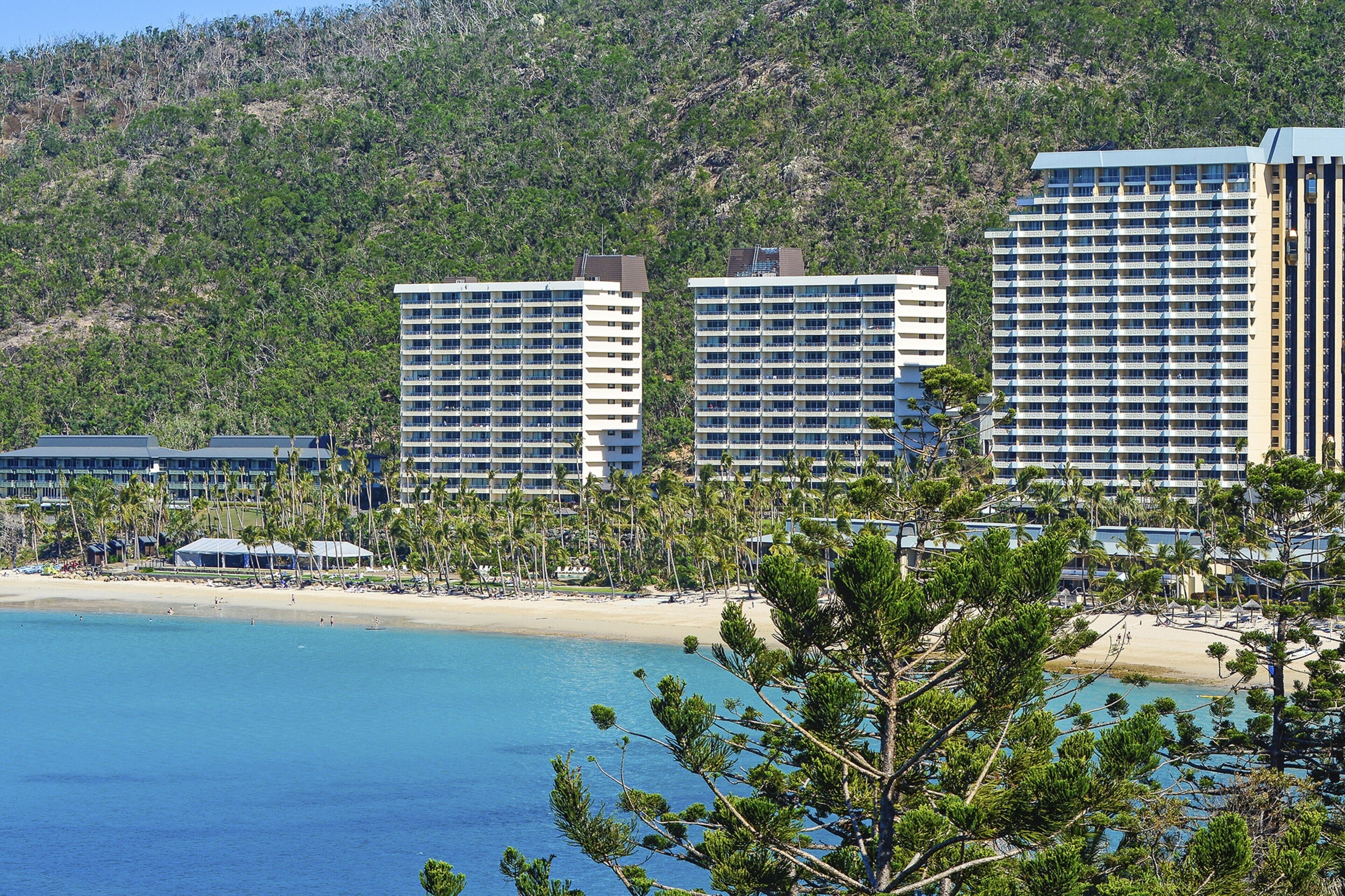 Um hotel à beira-mar com vários edifícios altos, uma praia arenosa e montanhas ao fundo.